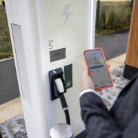 An over the shoulder point of view of an unrecognizable man using a specific app to check the charging status of his electric vehicle which he has placed on charge at a point in Newcastle upon Tyne in the North East of England